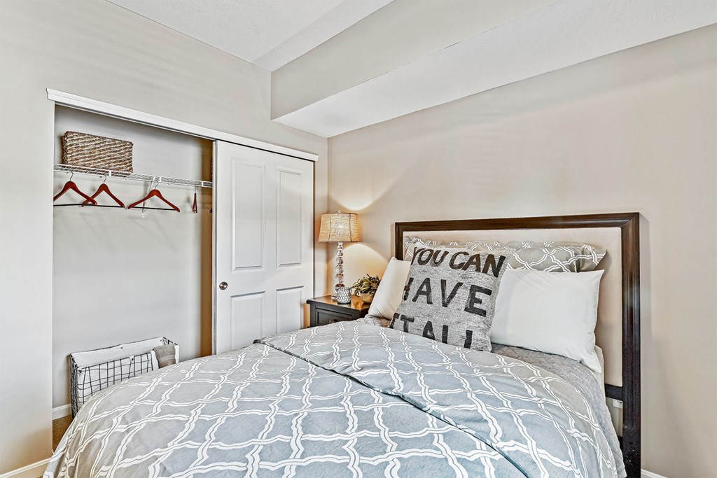 A bedroom with a bed, a lamp, and a pillow that says "You can have it all".