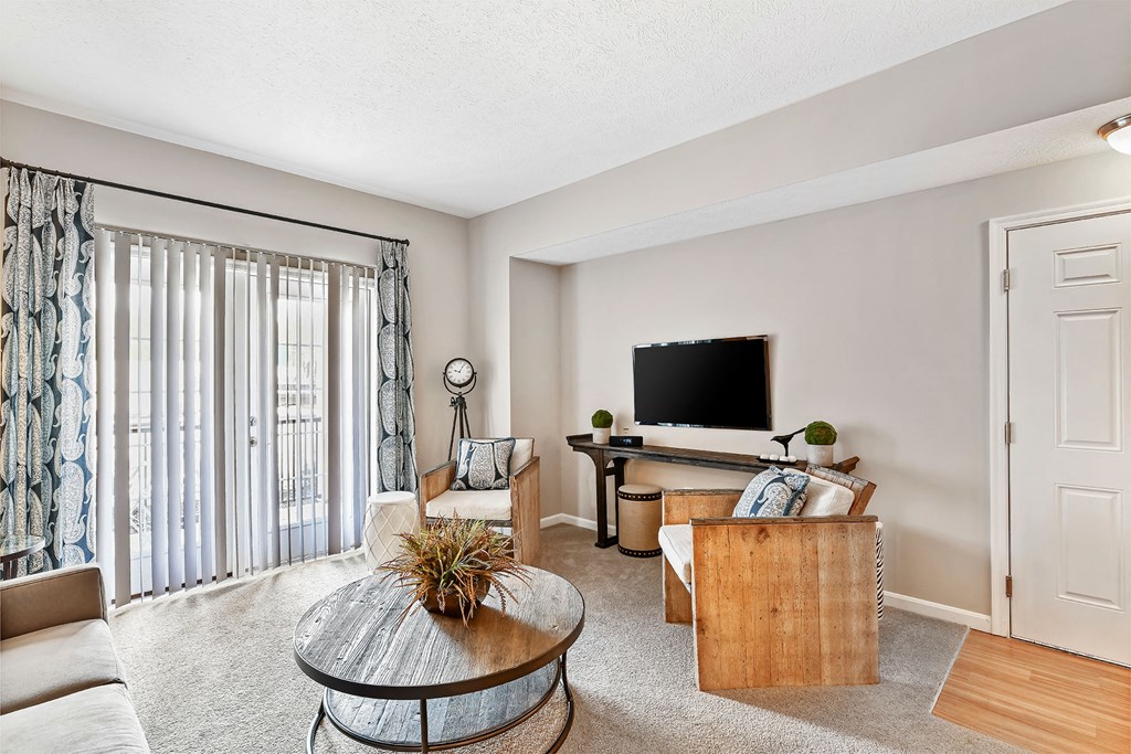 A living room with a television, a couch, a coffee table, and a window with curtains.