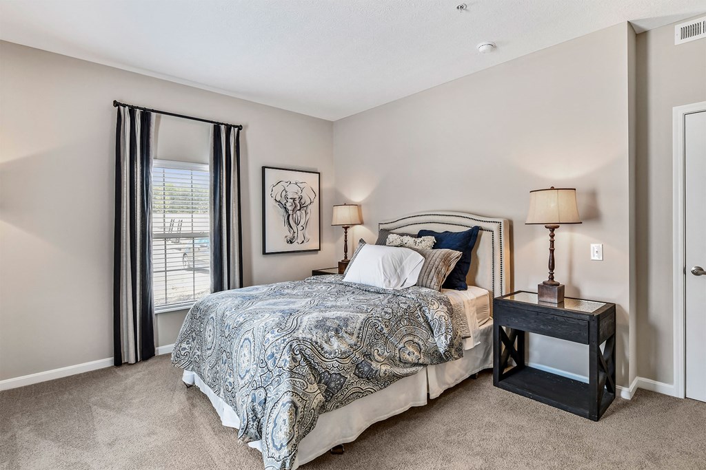 A bedroom with a bed, nightstand, and window with curtains.