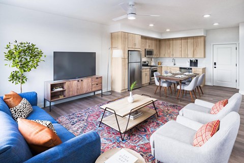 A living room with a blue couch, a wooden cabinet, a television, a dining table with chairs, and a potted plant.