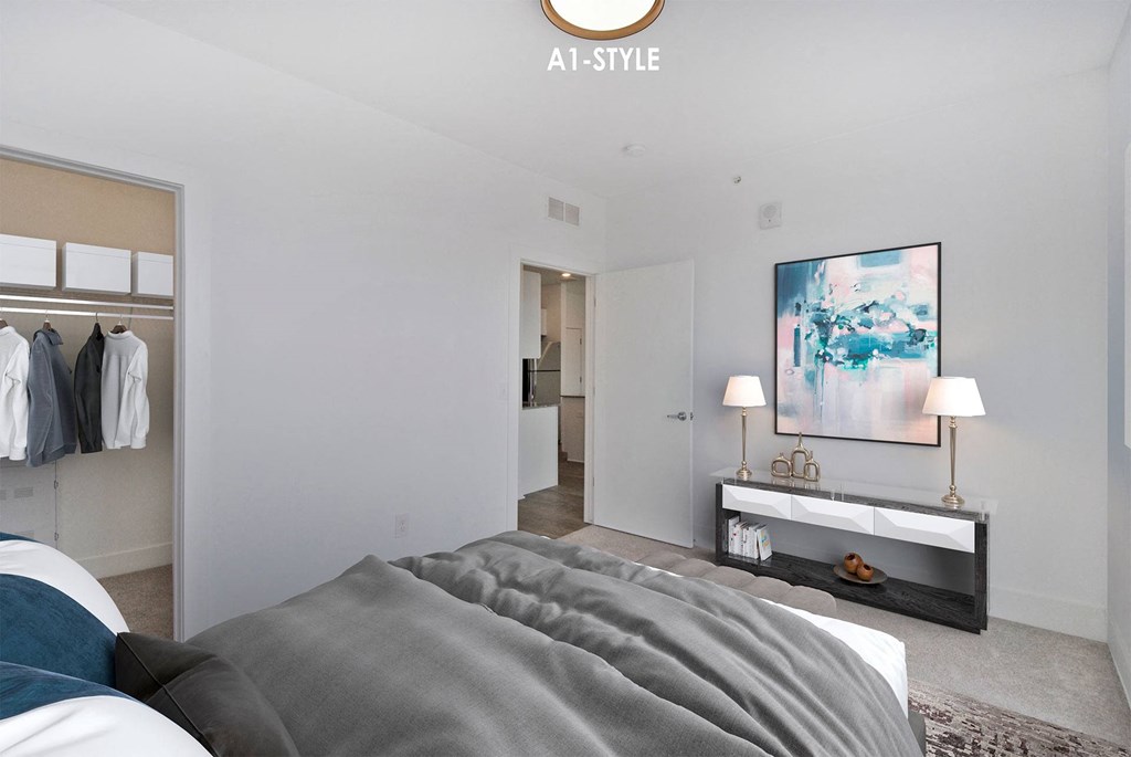 A bedroom with a bed, a clothing rack, and a painting on the wall.