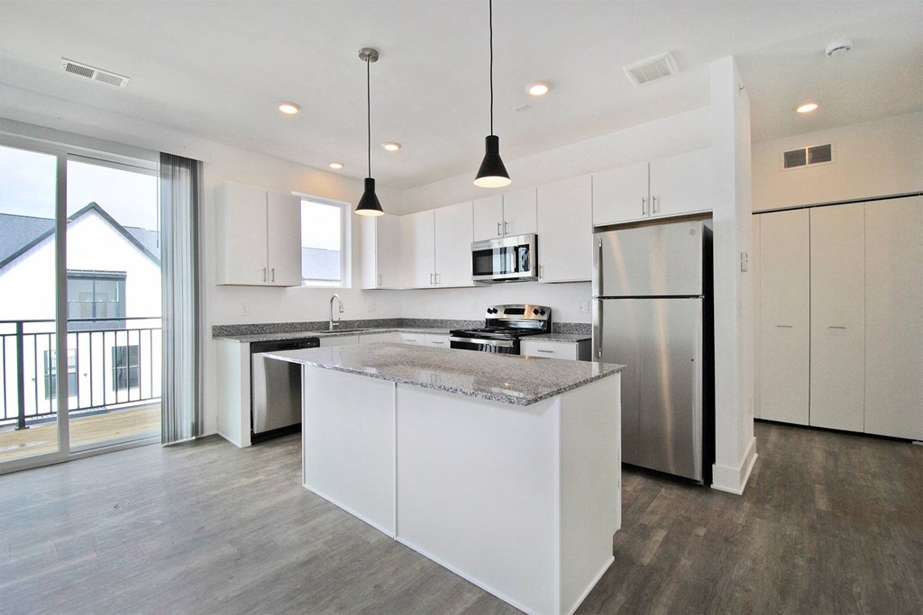 a white kitchen with a large island and stainless steel refrigerator
