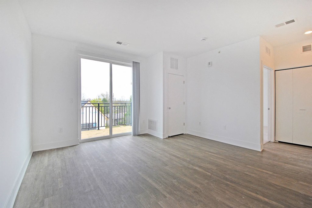 the living room of an empty apartment with wood flooring and a balcony