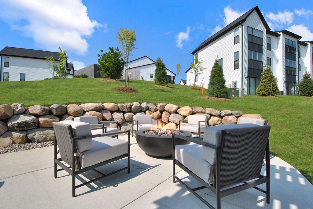 Two chairs are on a patio with a stone wall and a fire pit.