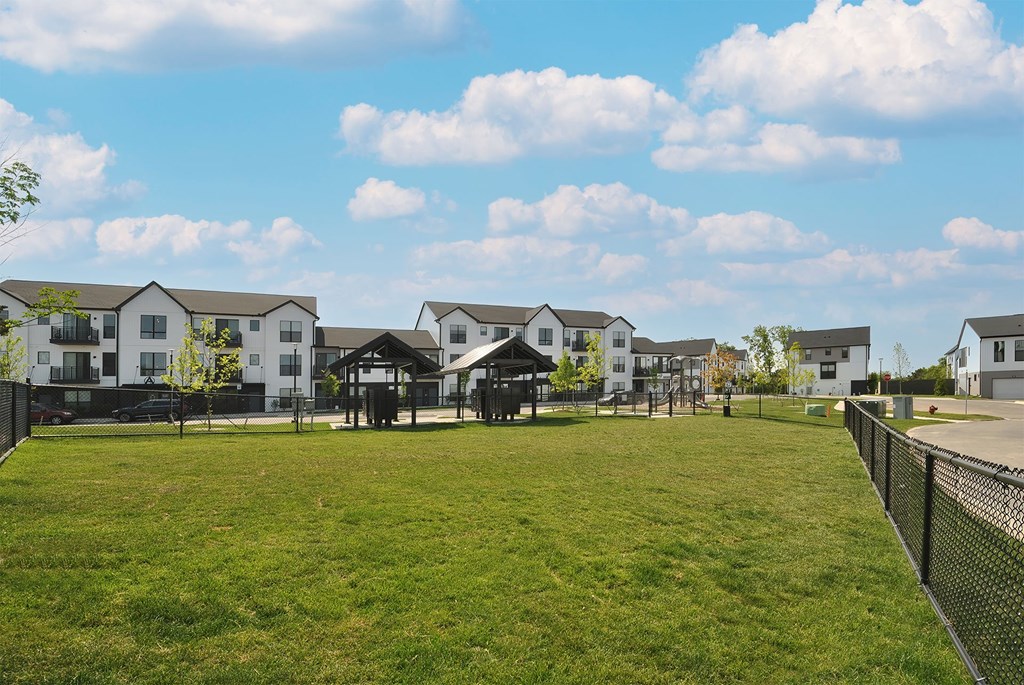A grassy field with a fence and houses in the background.