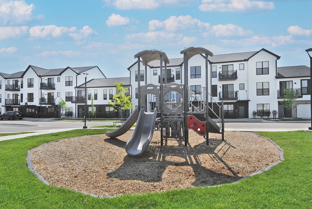 A playground with a slide and a red object in the middle of a gravel circle.