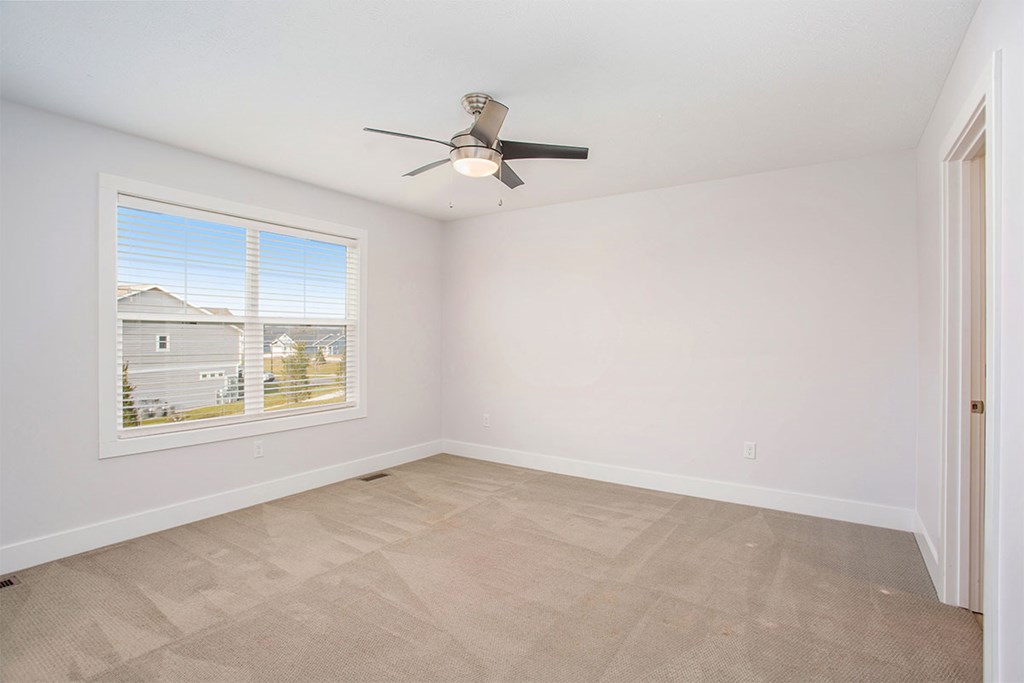A room with a ceiling fan and a window showing a view of houses.