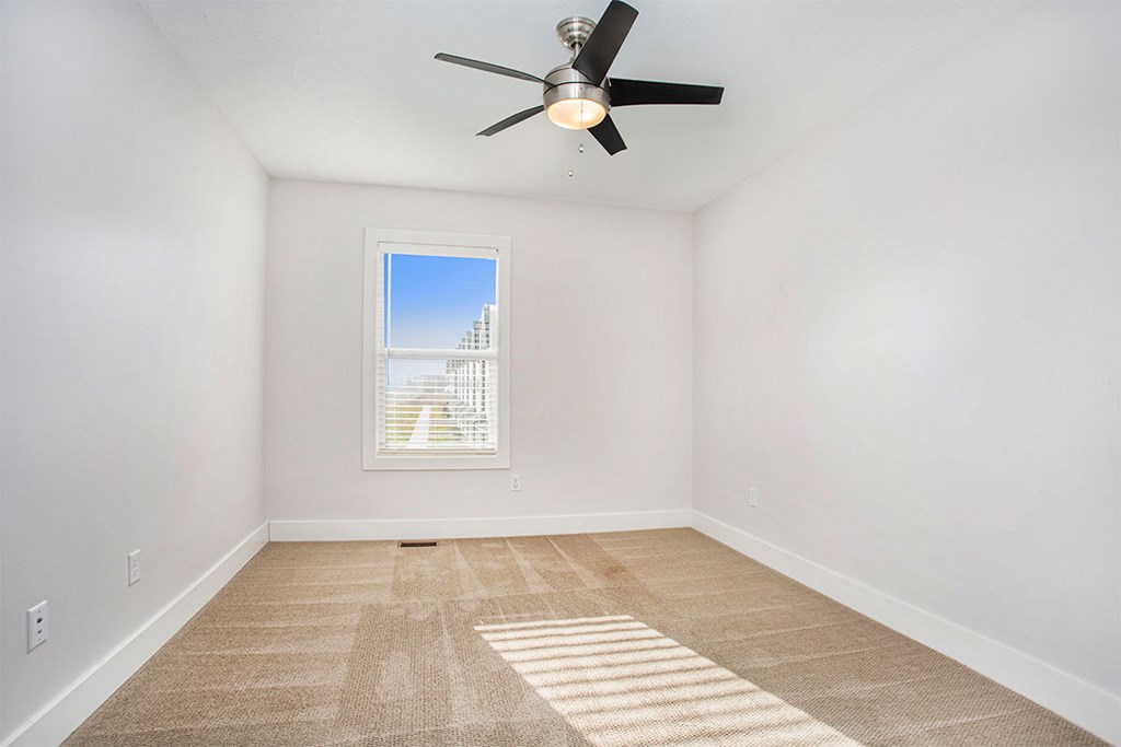 A room with a ceiling fan and a window letting in sunlight.