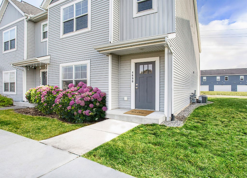 A grey house with a brown door and a small garden in front.
