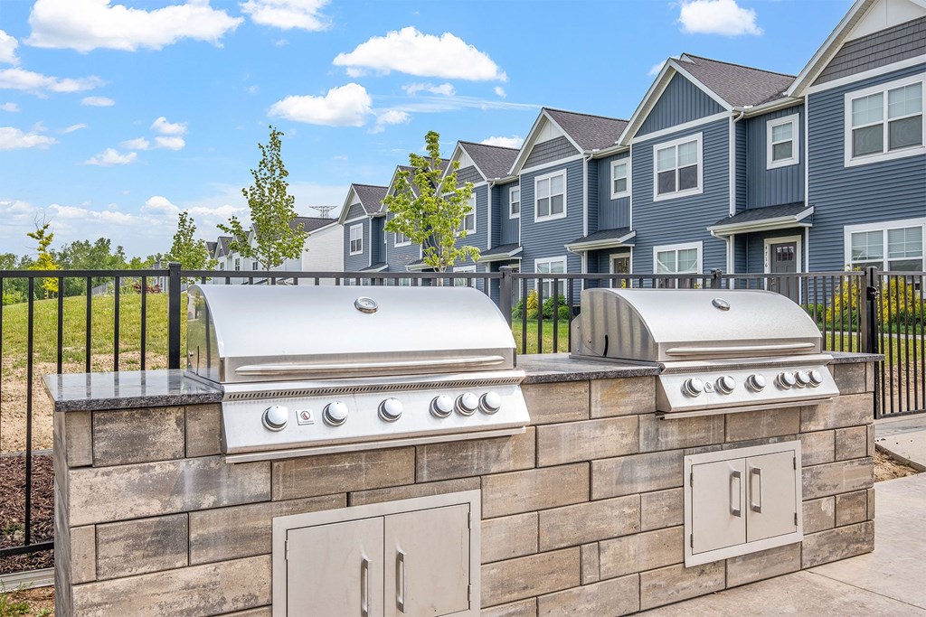 A stone wall with a grill on top and a fence in front of a house.