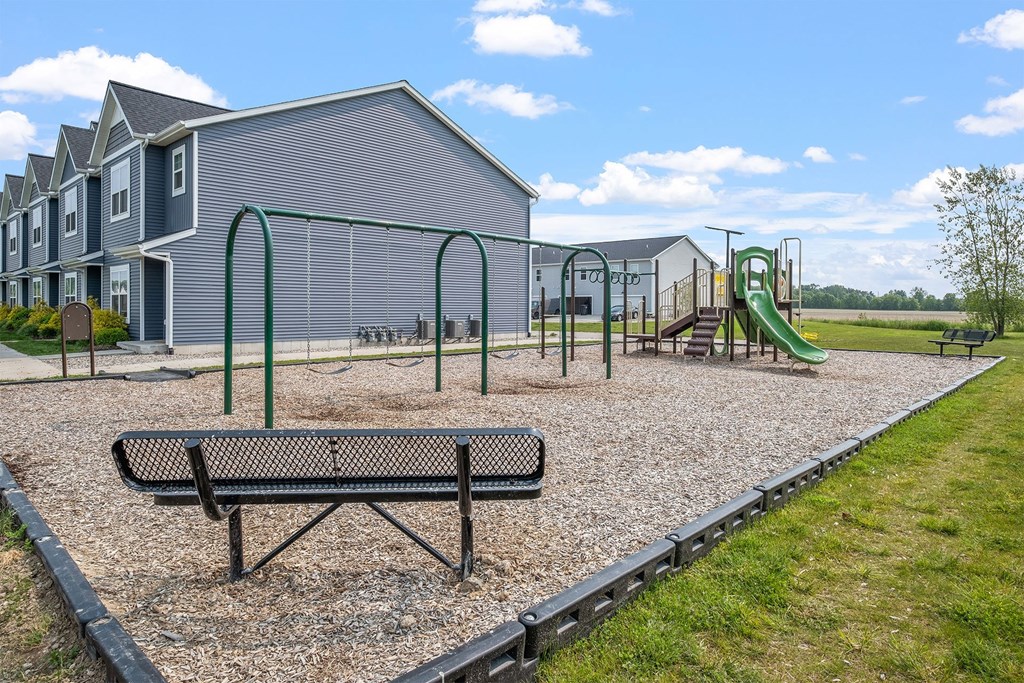 A playground with a green slide and a bench in front of a building.