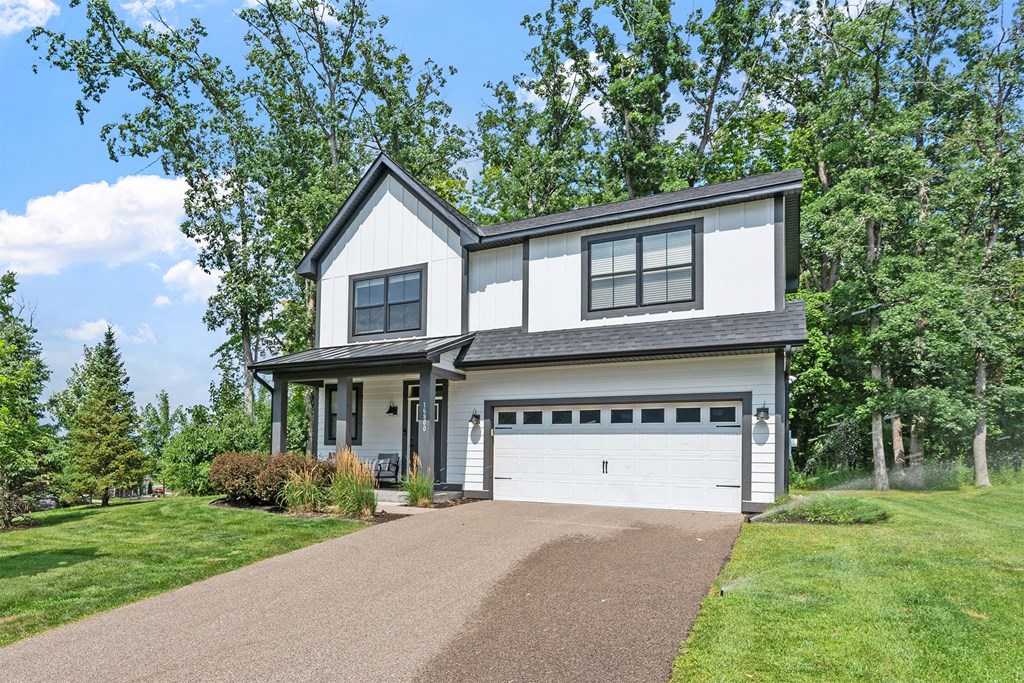 A two-story house with a garage is surrounded by greenery.