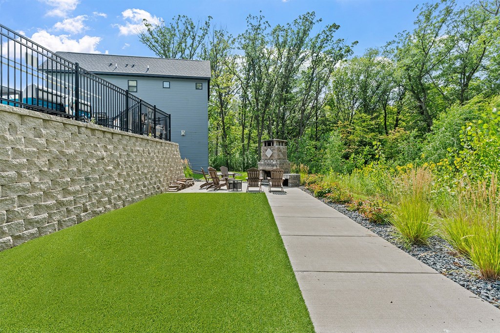 A backyard with a stone wall and a concrete walkway.
