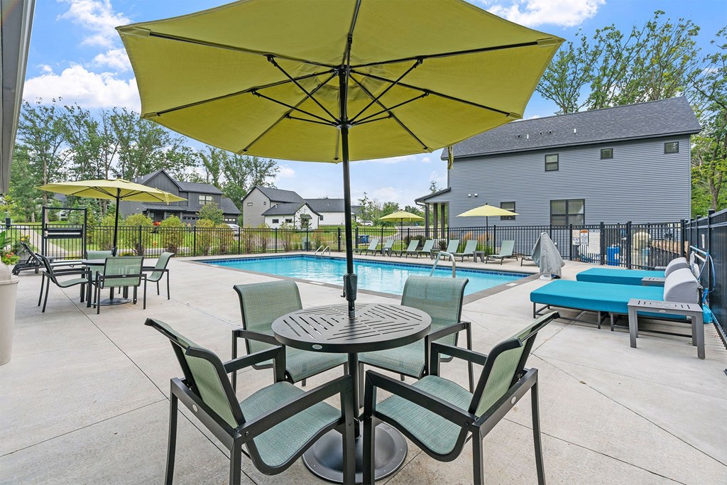 A yellow umbrella is in the middle of a table and chairs.