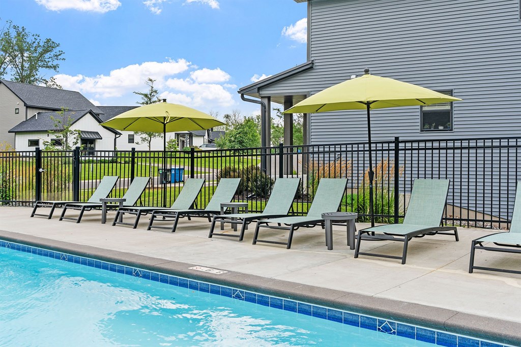 A pool with chairs and umbrellas in front of a house.