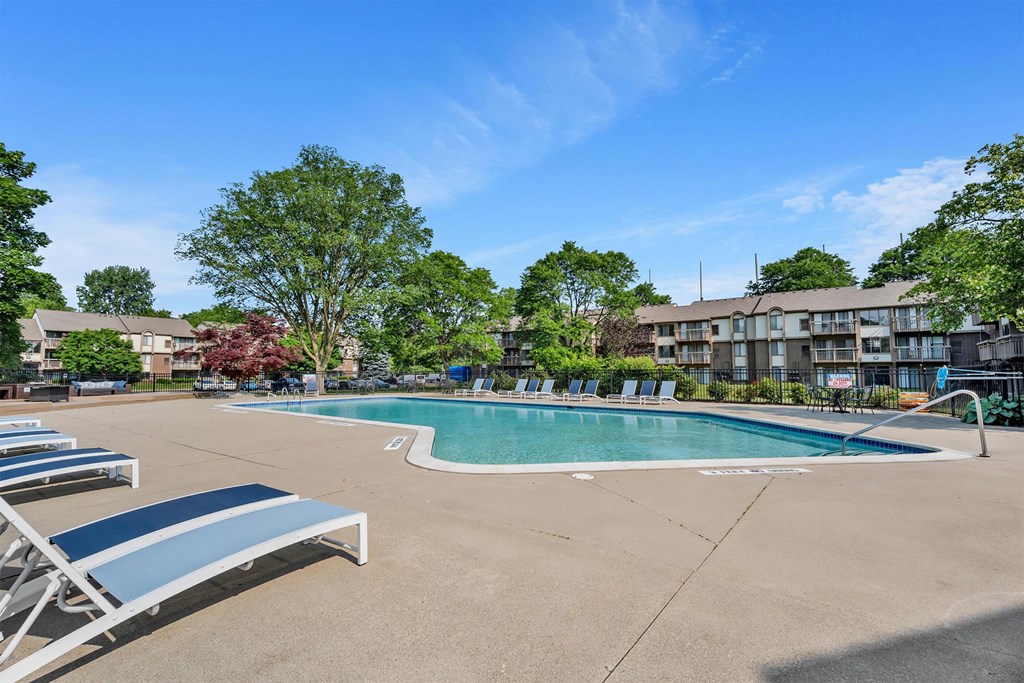 A pool with sun loungers and trees in the background.