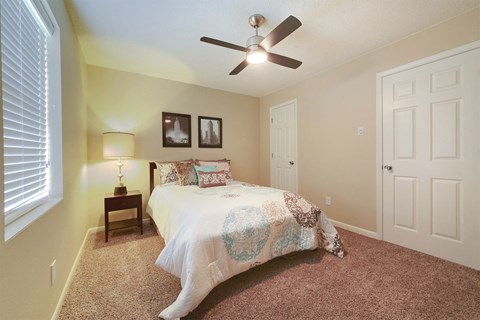 A bedroom with a bed, a ceiling fan, and two pictures on the wall.