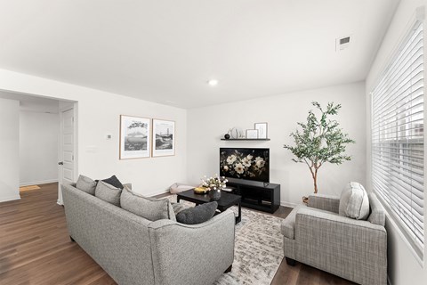 A living room with a grey couch, a small table with a vase of flowers, and a framed picture on the wall.