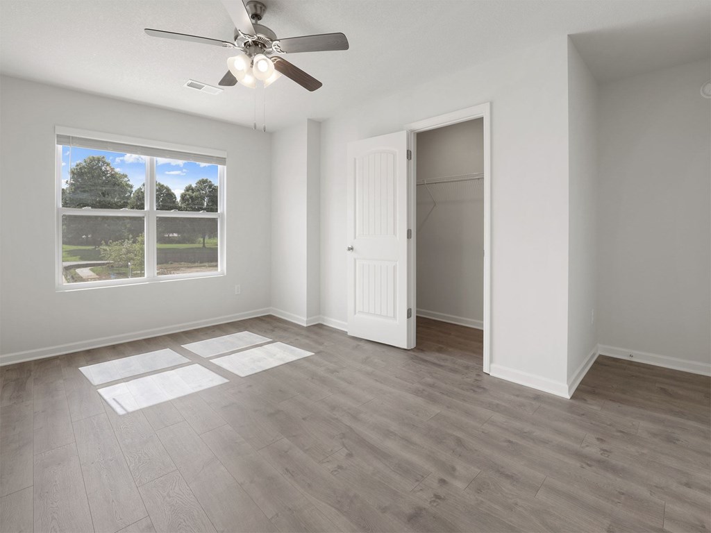A room with a ceiling fan and a large window overlooking a green area.