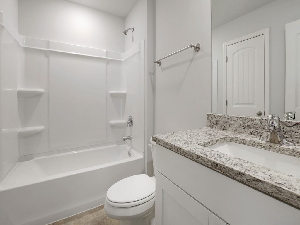 A white bathroom with a marble counter top and a white toilet.
