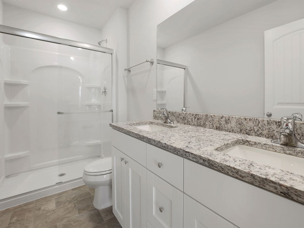 A white bathroom with a marble countertop and a walk-in shower.