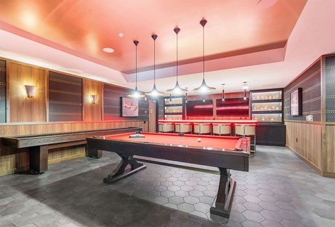 A pool table is in the middle of a room with a bench and lights hanging from the ceiling.