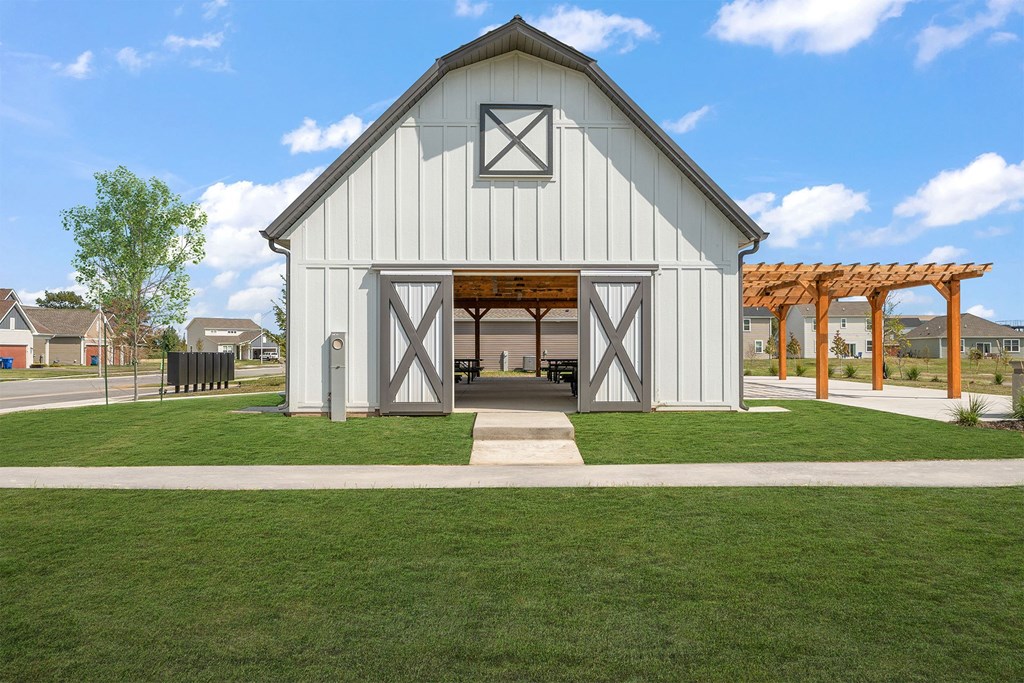A white barn-like building with a wooden roof and a green lawn in front.