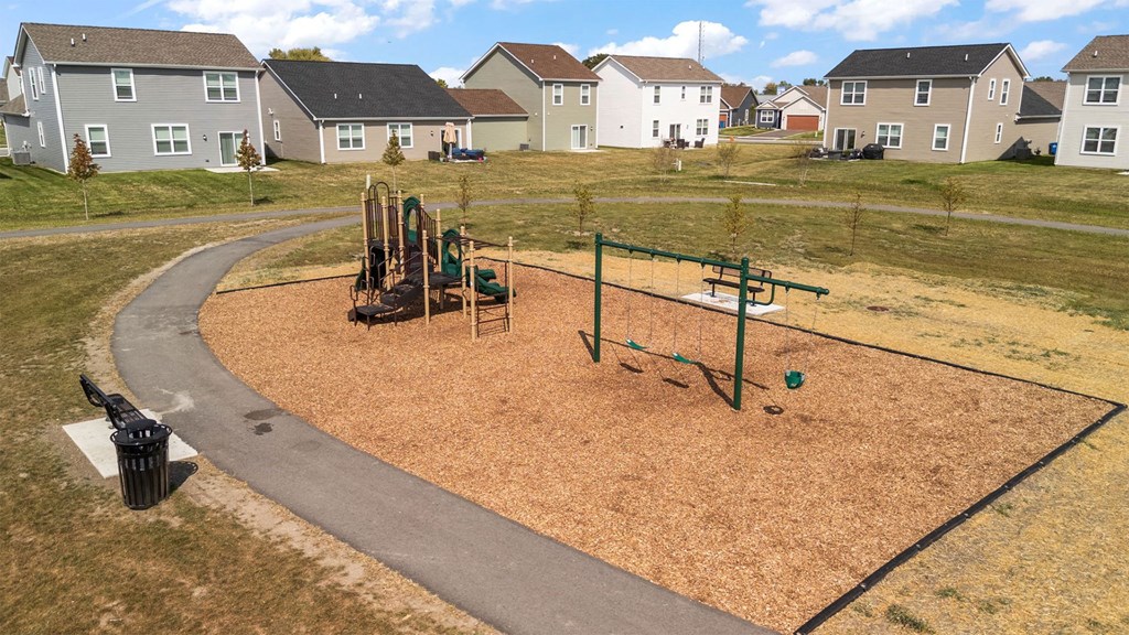 A playground with a slide, swings, and a seesaw in the middle of a grassy area.