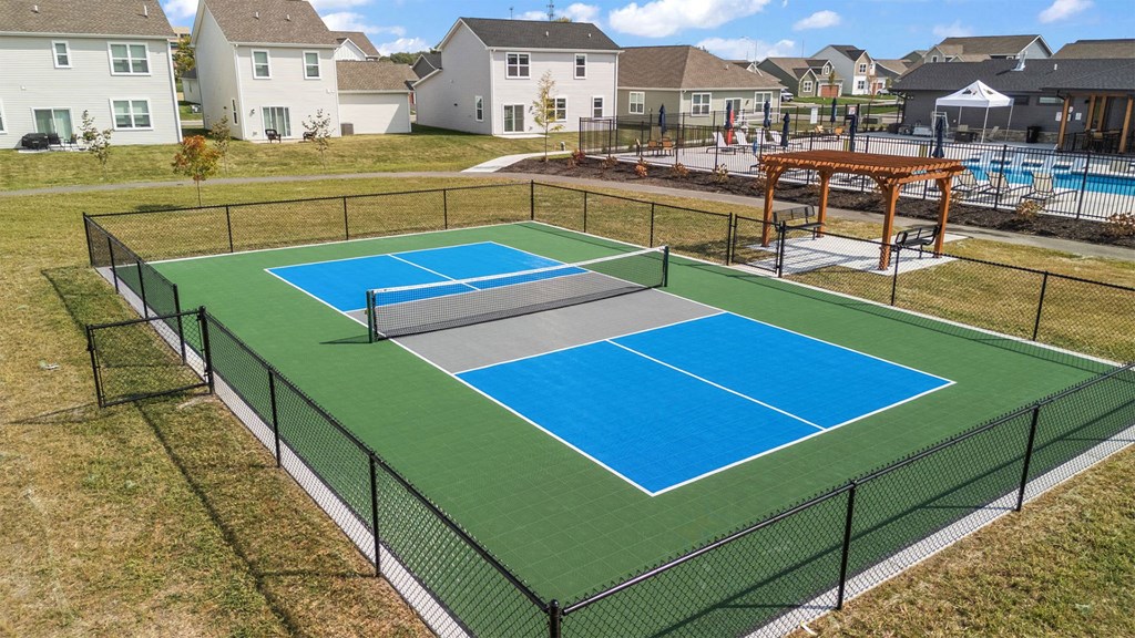 A tennis court with a green and blue surface surrounded by a black fence.