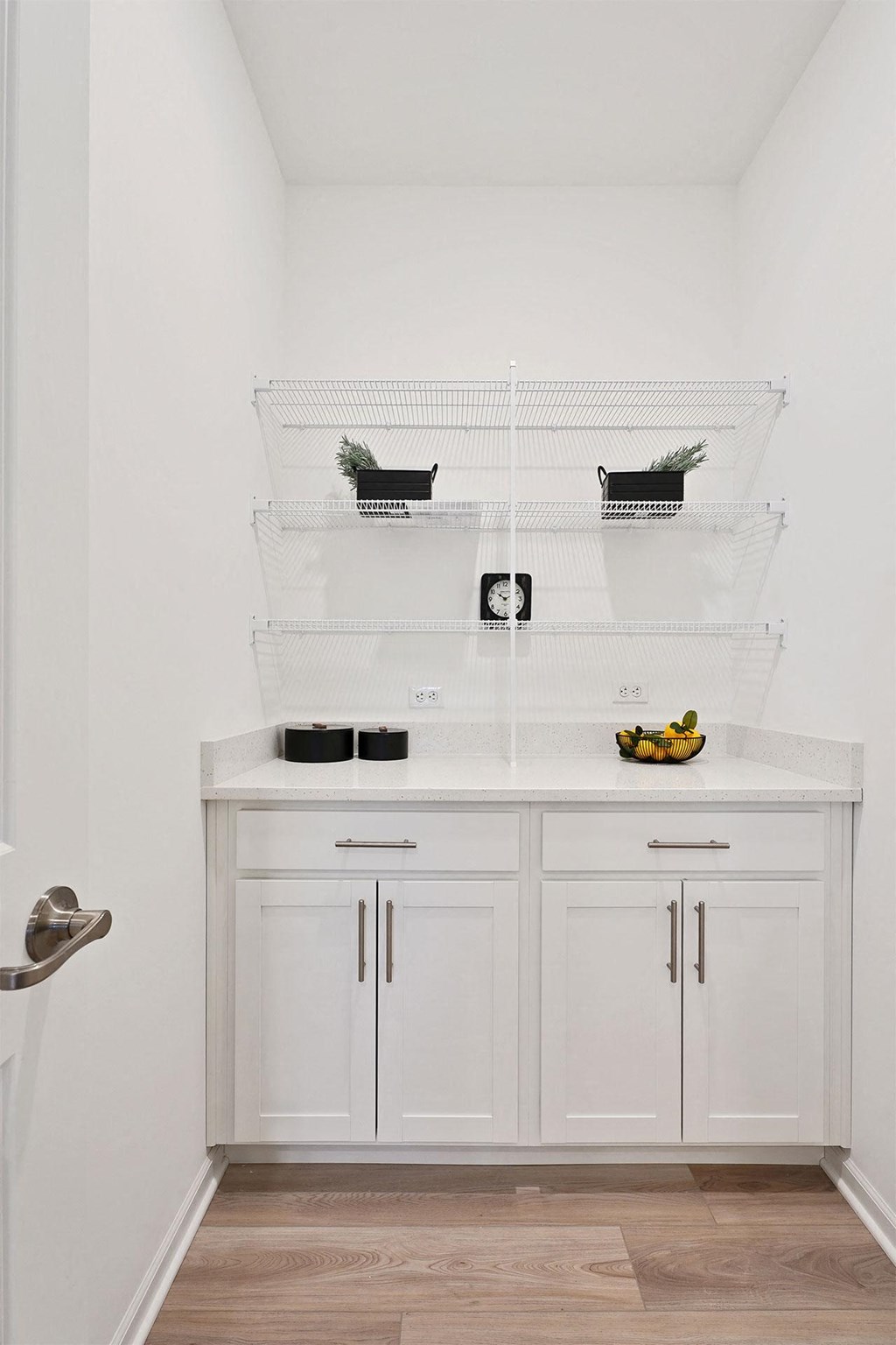A kitchen with white cabinets and a white countertop with a bowl of fruit on it.