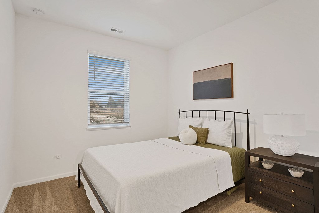 A bedroom with a bed, nightstand, and a window with blinds.