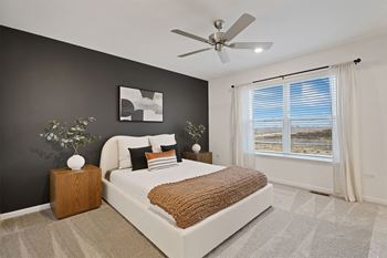 A bedroom with a large bed, a ceiling fan, and a window with blinds.