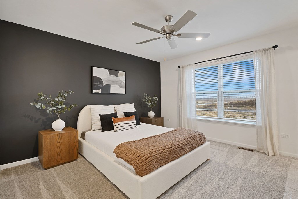 A bedroom with a large bed, a ceiling fan, and a window with blinds.