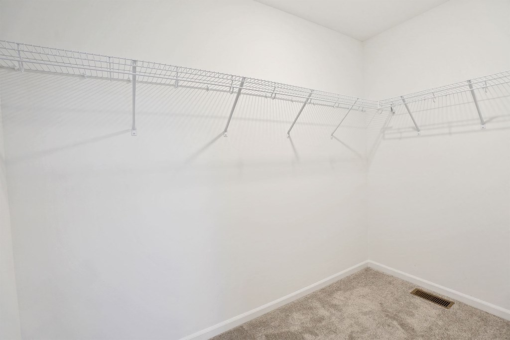 A white wall with a wire shelf and a carpeted floor.