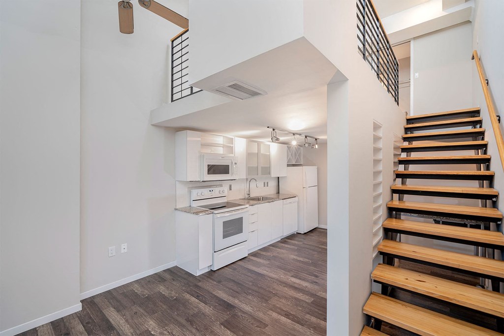 A modern kitchen with white appliances and wooden stairs.