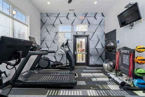 a gym with weights and cardio equipment and a wall with a television