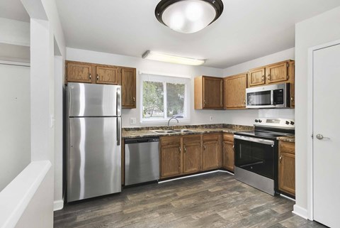 A kitchen with a stainless steel refrigerator, microwave, oven, and wooden cabinets.