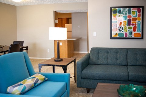 A blue chair with a pillow sits in a living room with a lamp and a couch.