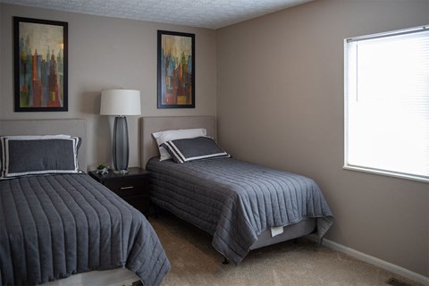 Two beds with grey bedspreads in a room with two lamps and two pictures on the wall.