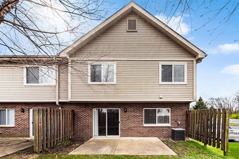 A house with a brown roof and a brick wall with a black trash can in front.