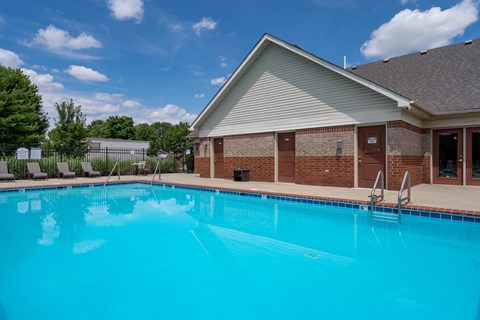 A swimming pool in front of a building with a pool house.
