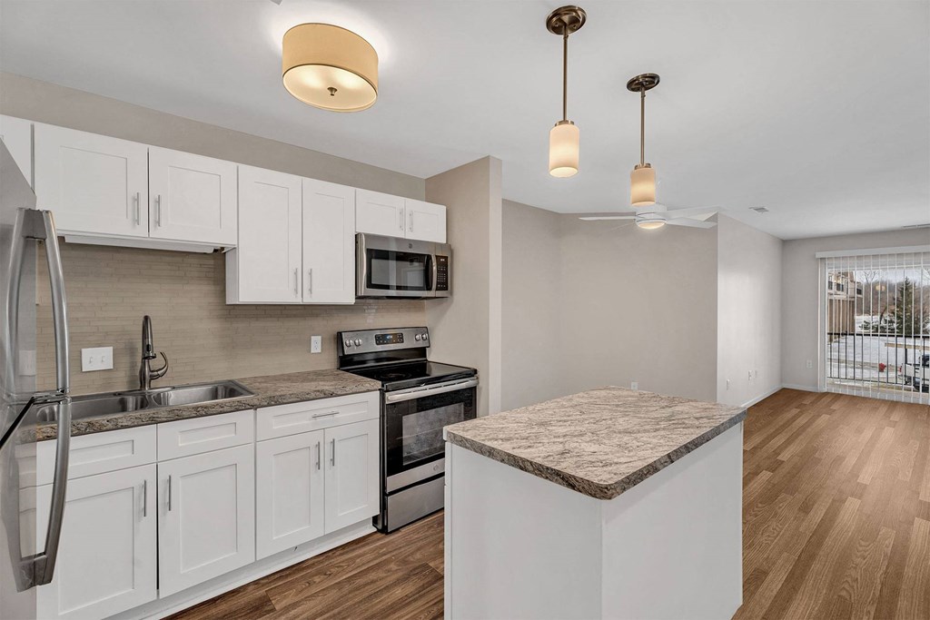 A kitchen with white cabinets and a marble island.