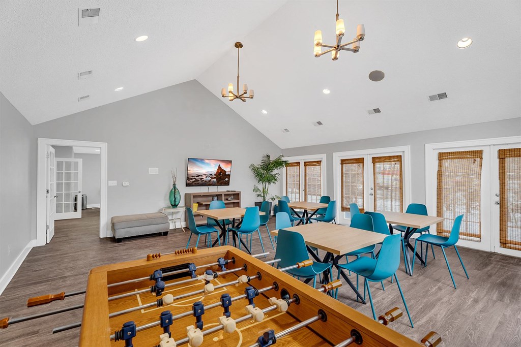 A foosball table is in the middle of a room with blue chairs and a TV in the background.