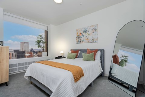 A bedroom with a large bed and a city view through the window.