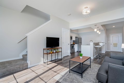 A living room with a grey couch, a coffee table, and a staircase.