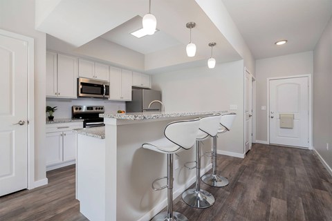 A kitchen with white cabinets and a bar area with stools.