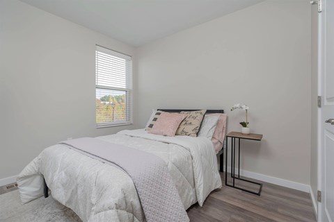 A bedroom with a bed, pillows, and a small table with a flower on it.