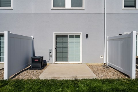 A grey house with a glass door and a black air conditioner unit.