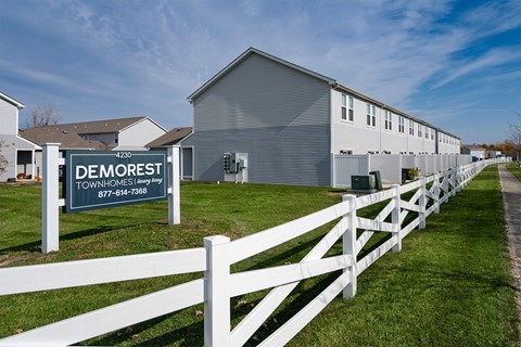 A sign for Demorest Townhomes stands in front of a white picket fence.