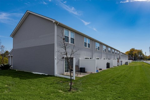 A long building with a grey facade and a tree in front of it.